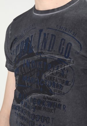 Primer plano de una persona que lleva una camiseta negra descolorida con una gran estrella desgastada y gráficos de texto en capas de azul y negro.