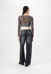 Transparente Bluse mit langen Ärmeln in einem braun-grauen Karomuster, kombiniert mit lässigen, lockeren, ausgewaschenen schwarzen Jeans. Klobige schwarze Schuhe vervollständigen den Look.