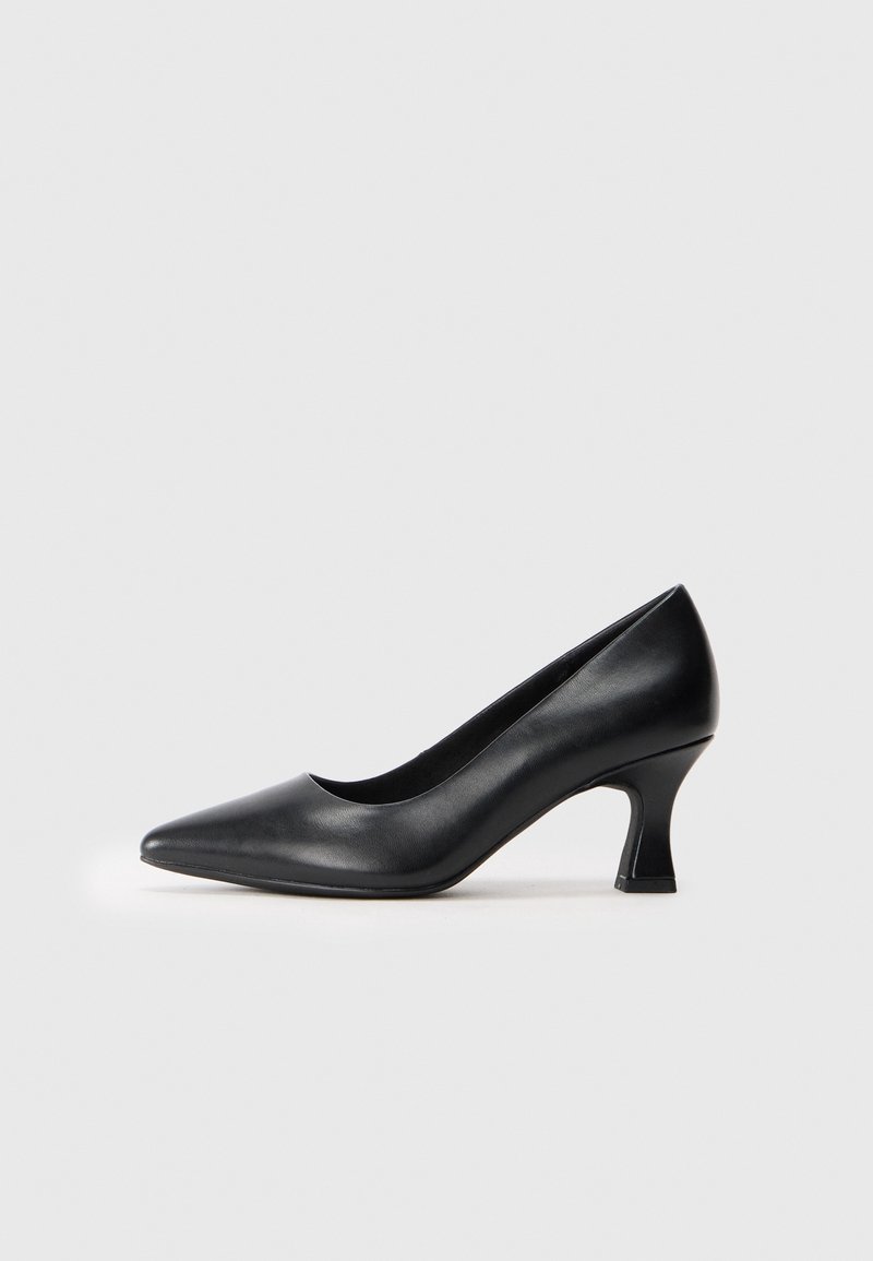 Escarpin en cuir noir à talon moyen, bout pointu et talon bloc incurvé sur un fond uni gris clair.