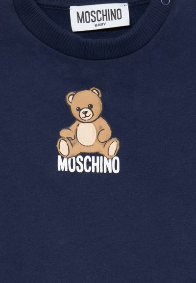 Sweat-shirt bleu marine avec un graphique de ours en dessin animé ayant un corps beige et un ventre crème, et le nom de la marque "MOSCHINO" en blanc en dessous.