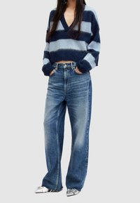 Krótszy dzianinowy sweter z szerokimi paskami w kolorze granatowym i jasnoniebieskim, z dekoltem w serek i szerokimi rękawami, zestawiony z wysokim stanem i luźnym krojem jasnoniebieskich dżinsów.