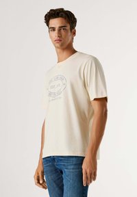 T-shirt en coton de couleur crème à manches courtes, avec un imprimé graphique bleu "Pepe Jeans London EST. 1973 Notting Hill" sur le devant.