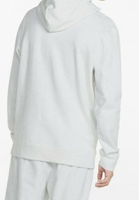 Persona vistiendo una sudadera de mezcla gris claro y pantalones a juego, mostrada desde atrás con una mano relajada a su lado.