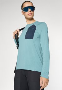 Langärmliges Sportshirt in Teal mit einer marineblauen Brusttasche. Verfügt über einen strukturierten Stoff und ein Logo-Detail auf der Vorderseite.