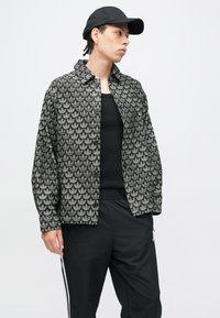 Fekete és szürke mintás kabát gallérral, levélmintával díszítve. Fekete trikó fölött viselve, fekete nadrággal és sapkával párosítva.