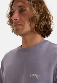 Ljuslila sweatshirt i bomull, med rund hals och ribbad mudd, med en liten vit logotyp på bröstet.