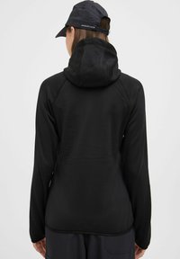 Zwarte sportjacket met capuchon, met een gladde textuur, lange mouwen en raglanontwerp. Achteraanzicht toont een minimalistische stijl en stikdetails.