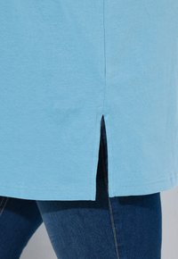 T-shirt in cotone azzurro chiaro con fessure laterali all'orlo, caratterizzato da una texture liscia e maniche corte, abbinato a jeans in denim blu scuro.