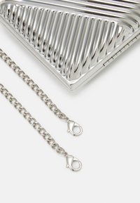 Metaliczna srebrna kopertówka z żłobionym wzornictwem, wyposażona w srebrny łańcuszek i zapięcia w kształcie homara dla bezpiecznego mocowania.