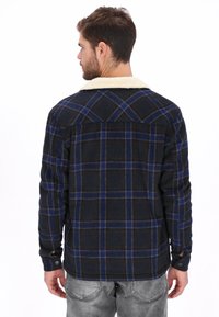 Camisa de cuadros en azul marino y negro con acentos azules y rojos, con cuello de borrego sintético crema y detalles de botones. Diseño de ajuste estándar.