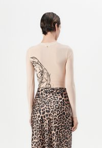 Naakt lange mouwen top met zwart grafisch ontwerp op de achterkant, gecombineerd met een satijnen rok met luipaardprint die verschillende bruin tinten toont.