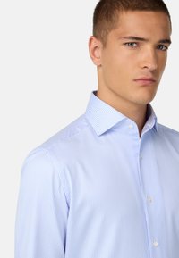 Gaišzils svītrots krekls ar pogām un izkliedētu apkakli, izgatavots no gludas auduma, ar mazām pogām un pieguļošu dizainu.