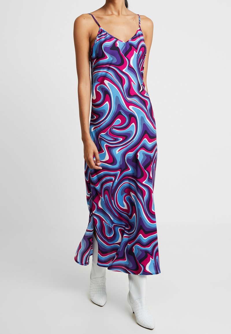 Robe multicolore avec des motifs tourbillonnants violets, bleus et roses, dotée de fines bretelles spaghetti et d'une fente latérale, confectionnée en tissu lisse.