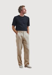 Zwarte korte mouwen top met een gestructureerd patroon, beige wijde broek, en lichtgewicht mesh schoenen, staand op een effen witte achtergrond.