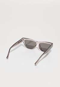 Occhiali da sole a forma di occhio di gatto con montatura trasparente rosa e lenti grigio scure. Presentano aste sottili e un marchio discreto sulla tempia.