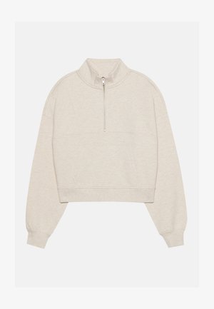 Lühendatud beež sweatshird, millel on kõrge krae ja poolne tõmblukk. Omab madalaid õlgu ja esist taskut, valmistatud pehmest struktuurse tööstusmaterjalist.