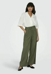 Blusa branca de mangas curtas combinada com calças largas verdes com cintura ajustável por cordão. Sapatilhas pretas completam o visual.