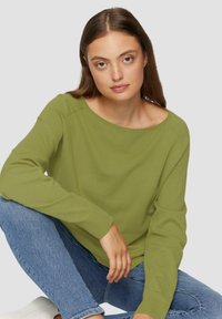 Groene sweatshirt met een wijde halslijn, lange mouwen en ribgebreide boorden. Gepaard met blauwe jeans, lijkt de stof zacht en comfortabel.