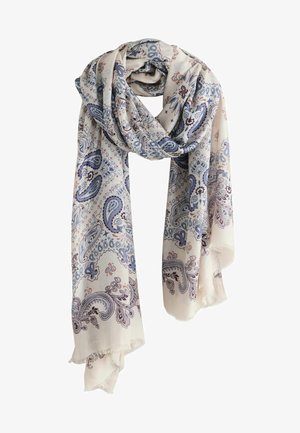 Kvinde iført brun strikket bralette, løse brune bukser samlet ved anklerne, bundet tørklæde med paisley-mønster og hæklede flade sko mod hvid baggrund.