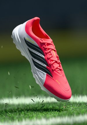 Scarpina da calcio rosa brillante con una parte superiore testurizzata, strisce nere, suola bianca e accenti gialli, progettata per offrire prestazioni su superfici in erba.