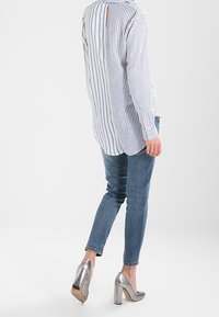Camicetta a maniche lunghe a righe blu e bianche, con dettaglio a occhiello sulla schiena, abbinata a jeans blu aderenti e scarpe con tacco alto argento.