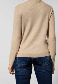 Beige stickad tröja med långa ärmar och en figursydd design, i kombination med mörkblå jeans som har bakfickor med detaljer och en texturerad yta.