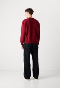 Felpa rossa con polsini e orlo a costine, abbinata a pantaloni scuri e larghi. Entrambi i capi hanno dettagli minimi e linee pulite.