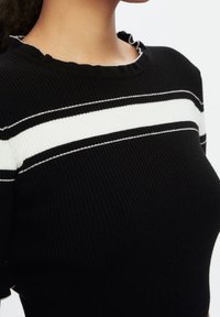Top negro de canalé con rayas horizontales blancas. Presenta un escote redondo con un borde rizado y mangas cortas. Textura suave.