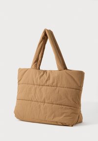 Hnědá pufovaná látková taška s širokými uchy, vystavená na jednobarevném bílém pozadí.