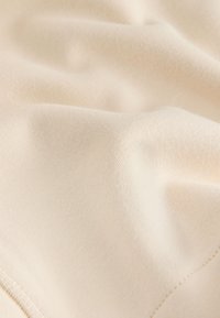 Lichtbeige stof met een gladde textuur, voorzien van subtiele stiksel details. Het materiaal oogt zacht en licht rekbaar.