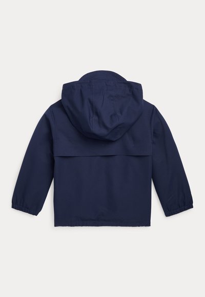 Mornarsko modra jakna s kapuco, dolge rokave in elastične manšete. Hrbtna stran ima pravokotno oblikovanje jorka za dodatno podrobnost.