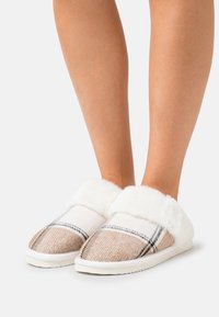 Tan and white plaid slippers with a white faux fur cuff and a flat sole. Soft texture with a rounded toe design.
