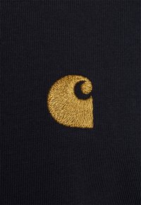Navy textile with a golden embroidered logo featuring a swirl design, showcasing smooth texture and detailed stitching.