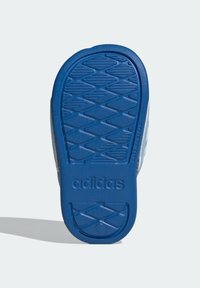 Blå gummisula med ett diamantmönster och präglad "adidas"-logotyp. Ljusgrå sidodetaljer sträcker sig uppåt från hälen.