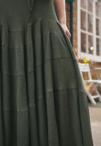 Dark green, textured dress with a tiered design. Fabric appears lightweight with subtle, horizontal pleats. No visible fastenings.