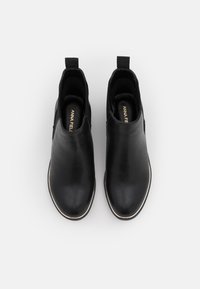 Botines de piel negra con textura suave, paneles laterales elásticos y una suela delgada blanca. Lengüeta en la parte trasera para facilitar su colocación.