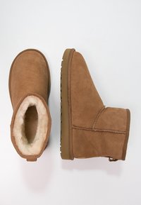 Botines de ante marrón con un suave forro de borreguito beige y suelas de goma. Punta redondeada y costuras a lo largo de las uniones.