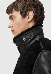 Black leather jacket with a shearling collar, featuring a snap closure and textured fabric. Smooth finish, close-fitting design.