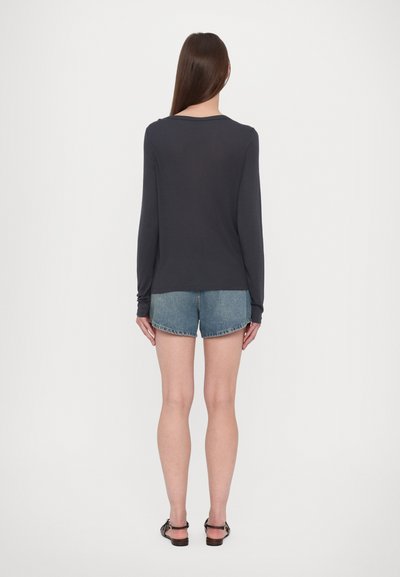 Langärmliges, dunkelgraues Oberteil aus leichtem Stoff, lässige Passform. Kombiniert mit hellblauen Denim-Shorts mit leicht ausgefranstem Saum und schwarzen Sandalen.