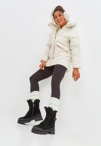 Chaqueta acolchada color crema con capucha, leggins negros y botas de pelo negras. Medias de punto blancas añaden contraste en la zona de las pantorrillas.