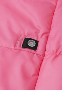 Różowa pikowana sekcja kurtki z błyszczącym wykończeniem, wyposażona w czarny pasek z tkaniny i przezroczysty zatrzask, z widocznymi detalami przeszyć.