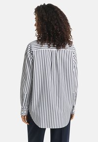 Strukturierte Baumwollbluse mit vertikalen navyblauen und weißen Streifen, langen Ärmeln und abgerundetem Saum. Enthält einen Rückenfalten und geknöpfte Manschetten.