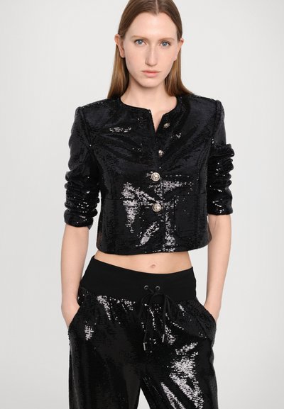 Cropped black sequin jacket with a round neckline, three-button front closure, and ruched sleeves. Paired with matching sequin joggers.