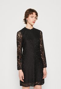 Black lace dress with long sleeves, scalloped neckline, intricate floral patterns, and a slightly flared hem. Textured design throughout.