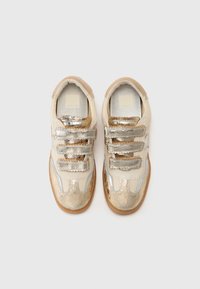 Sneaker in pelle crema con dettagli metallici dorati. Tre cinturini argentati sulla parte anteriore, suole in gomma texturizzata e design a punta arrotondata.