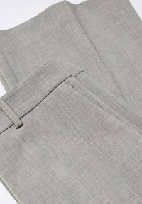Pantalon gris clair sur mesure plié montrant la ceinture, la passants de ceinture et la texture du tissu.