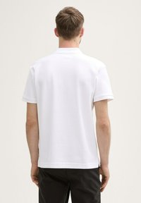 Hvid kortærmet poloshirt med tekstureret stof, flad krave og sideslids. Ingen synlige mønstre eller hardwaredetaljer.