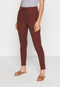 Viininpunaiset kapeat housut, joissa on naruvarsi, sivutaskut ja sileä pinta, yhdistettynä ruskeisiin liukumäkipahkoihin. Raidoitettu paita näkyvissä.