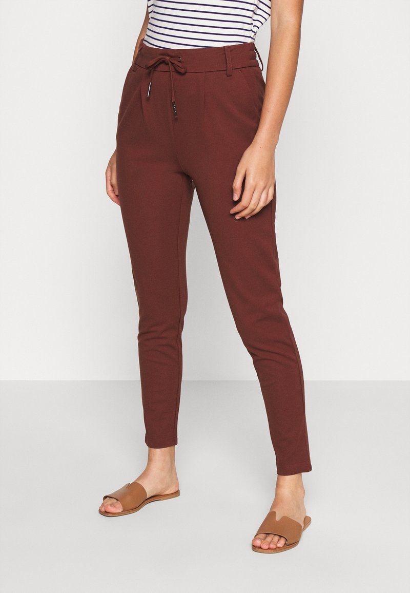 Viininpunaiset kapeat housut, joissa on naruvarsi, sivutaskut ja sileä pinta, yhdistettynä ruskeisiin liukumäkipahkoihin. Raidoitettu paita näkyvissä.