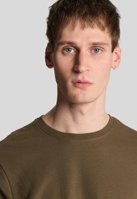 T-shirt in cotone verde oliva con scollatura rotonda e maniche corte, caratterizzato da una superficie testurizzata e dettagli di cucitura minimi.
